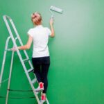 A l'aide de son escabeau, une jeune femme applique une couleur verte sur son mur