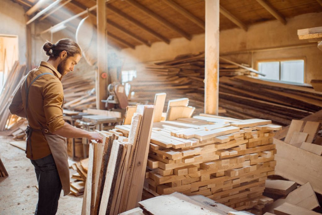 Un menuisier chosit une planchede bois massif dans son atelier